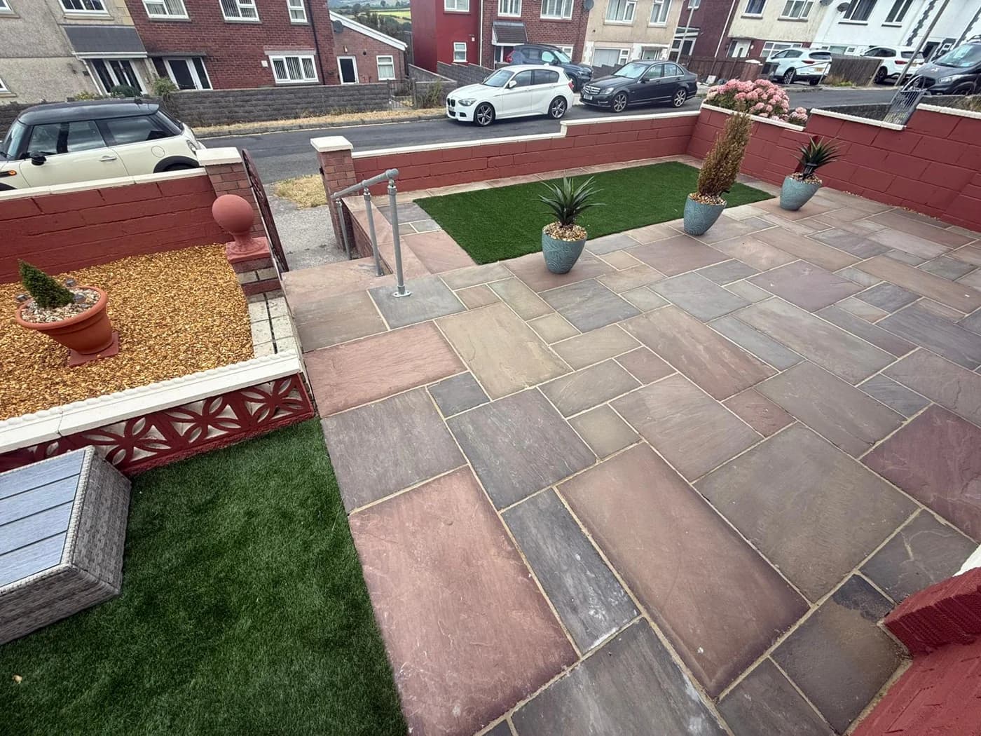 Raised front garden with Indian sandstone paving, painted boundary walls, brick pillars, artificial grass and a metal handrail to the steps